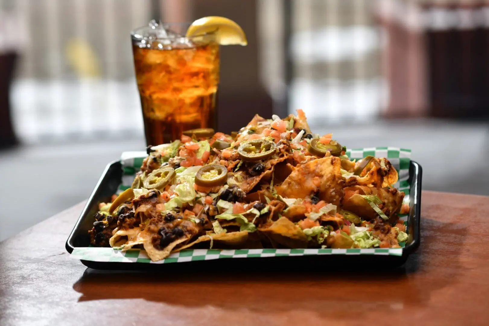 A tray of nachos and a drink on the table.