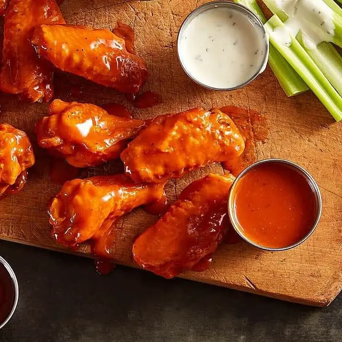 Buffalo wings on a cutting board with celery and dipping sauce.